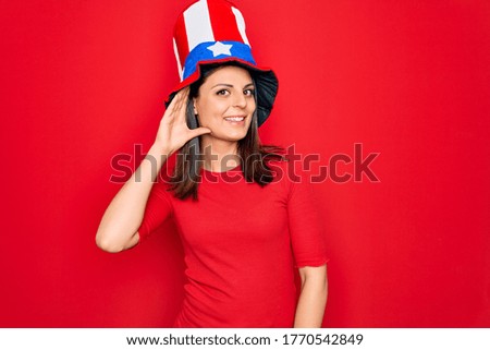 Young beautiful brunette woman wearing united states hat celebrating independence day smiling with hand over ear listening an hearing to rumor or gossip. Deafness concept.