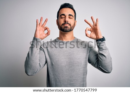 Young handsome man with beard wearing casual sweater standing over white background relax and smiling with eyes closed doing meditation gesture with fingers. Yoga concept.