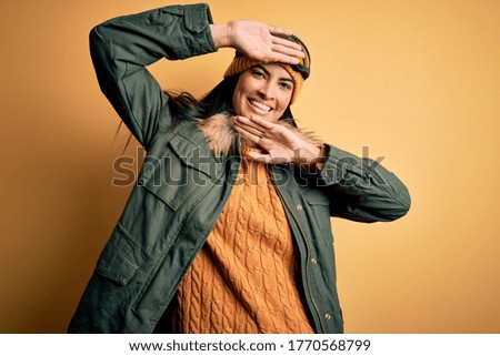 Young beautiful hispanic woman wearing ski glasses and coat for winter weather Smiling cheerful playing peek a boo with hands showing face. Surprised and exited
