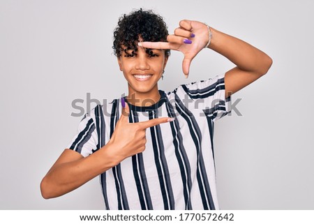 Beautiful african american afro woman wearing casual striped t-shirt over white background smiling making frame with hands and fingers with happy face. Creativity and photography concept.