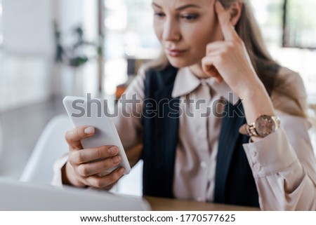 selective focus of displeased businesswoman using smartphone in office