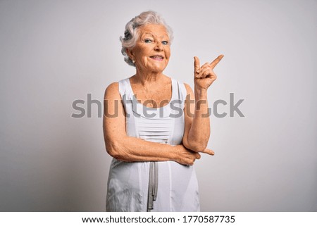 Senior beautiful grey-haired woman wearing casual summer dress over white background with a big smile on face, pointing with hand and finger to the side looking at the camera.