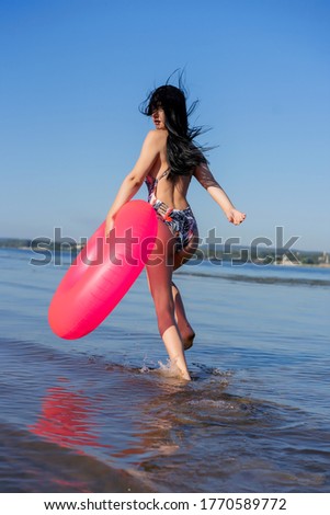 dark-haired beautiful girl with a pink rubber ring runs along the beach
