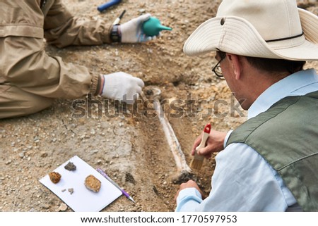 two paleontologists extract fossilized bone from the ground in the desert, focus on a close researcher Royalty-Free Stock Photo #1770597953