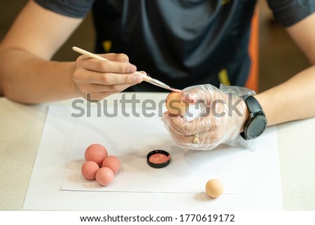 A hand in protective gloves painting the balls. Men's hands hold a detail and brush and paint the balls pink. Step 1