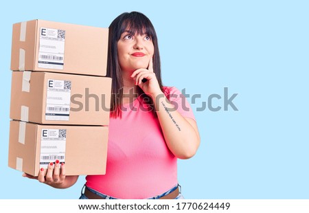 Young plus size woman holding delivery package serious face thinking about question with hand on chin, thoughtful about confusing idea 