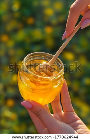 a girl holds a jar of honey on the palm of her hand against a background of yellow flowers