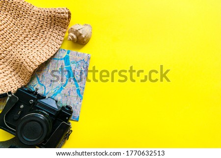 Summer travel accessories on yellow background. Flat lay beach hat, vintage camera, plane, map, passport, sunglasses, seashells and green leaves. Holiday vacation trip planning concept