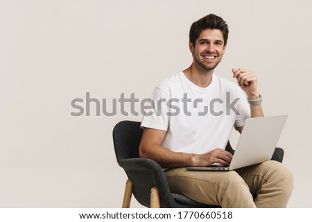 Portrait of unshaven laughing man working with laptop while sitting on armchair isolated over white background Royalty-Free Stock Photo #1770660518