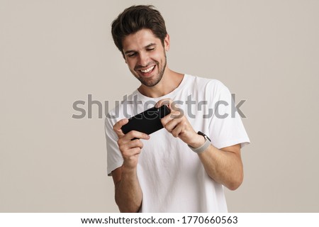 Portrait of unshaven excited man playing online game on mobile phone isolated over white background