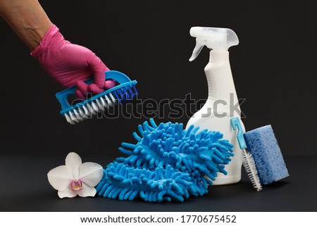 Plastic bottle of dishwashing liquid, a rag, an orchid flower and a hand with a brush on the black background. Washing and cleaning set.