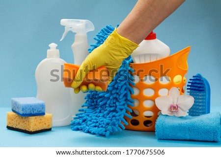 Woman's hand in a yellow nitrile glove holding a sponge with a washing and cleaning set on the blue background.