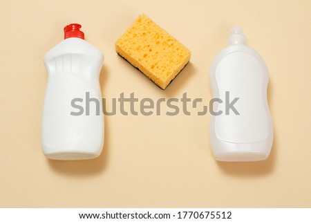 Plastic bottles of dishwashing liquid, detergent for microwave ovens and stoves and a sponge on a beige background. Top view. Washing and cleaning set.