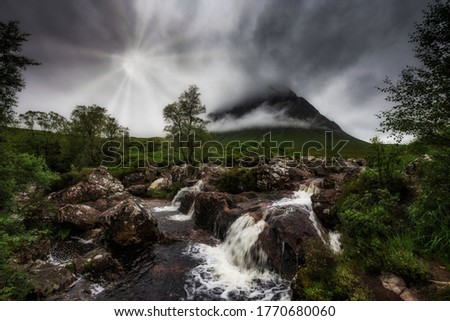 River coupall waterfalls with the Buachaillie Etive mor mountain in the background in clouds with sun burst coming through. Glencoe, highlands, Scotland.