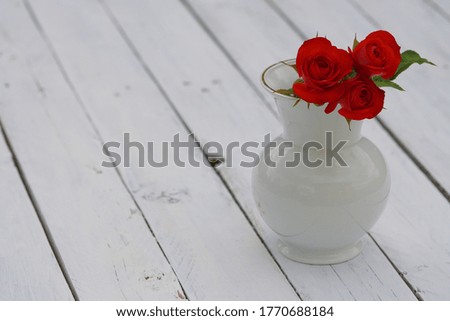 Red roses in white vase on white old table