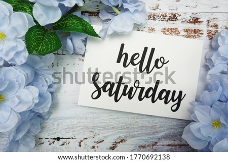 Hello Saturday Card with Blooming flower on wooden background