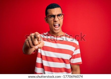 Young handsome african american man wearing casual striped t-shirt and glasses pointing displeased and frustrated to the camera, angry and furious with you