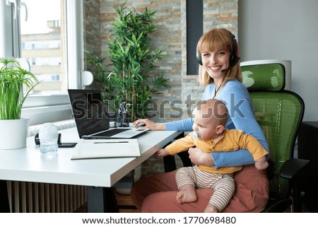 Responsible parent sitting in the office and holding her child while working