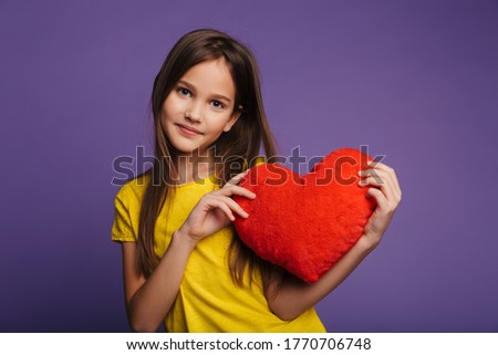 Photo of happy beautiful girl holding soft toy heart and smiling isolated over purple background