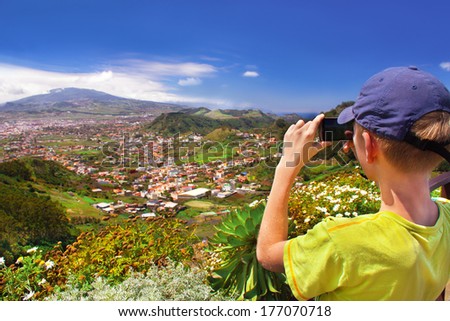 Caucasian boy blogging is taking photos by smartphone camera of the landscape - mountain valley (dale). Summer vacation trip. Tenerife, Canary islands, Spain. Outdoor. 