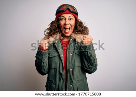 Middle age skier woman wearing snow sportswear and ski goggles over white background celebrating surprised and amazed for success with arms raised and open eyes. Winner concept.