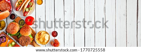 Summer BBQ food table scene with hot dog and hamburger buffet. Above view corner border over a white wood banner background. Copy space.
