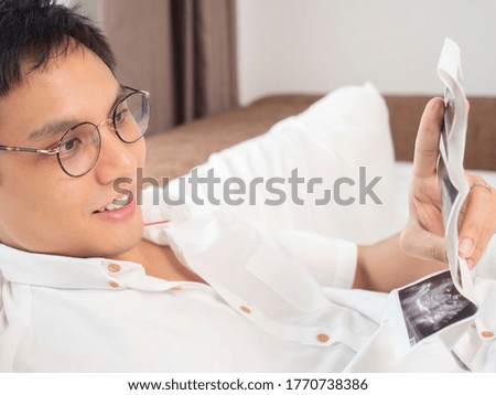 Asian man looking at pregnant ultrasound x-ray film in white bed room.