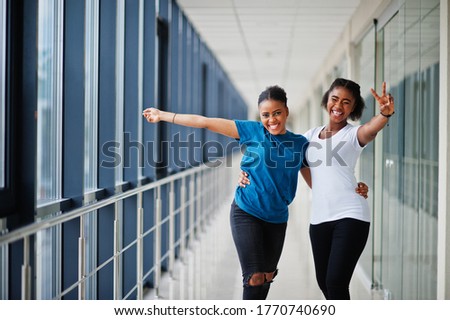 Two african woman friends in t-shirts posed indoor together.
