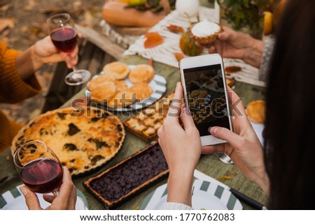 A young girl takes a photo of a festive family table on a smartphone. Autumn brunch in the backyard.