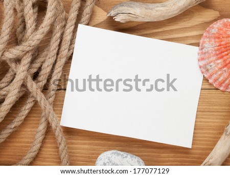 Blank photo frame with ship rope and seashells over wooden background