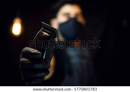 barber holding a black hair clipper wearing a black face mask on dark background Royalty-Free Stock Photo #1770803783