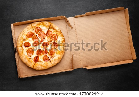 Pizza in a cardboard box on a dark chalkboard. Space for your text. Top view of pizza package. Pizza delivery. Royalty-Free Stock Photo #1770829916