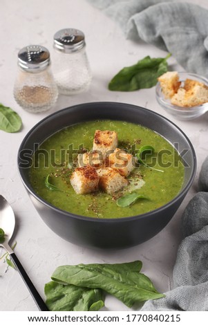 Green spinach puree soup served with croutonsin a dark bowl on a gray concrete background, Closeup, Vertical format