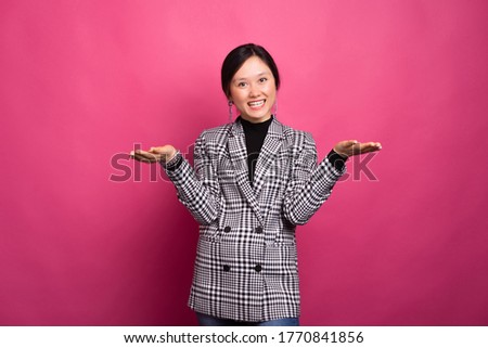 Smiling young woman is standing over pink background with arms opened for a hug or for presenting something