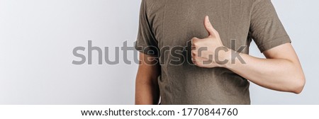Nice job man, like it. Pleased good-looking happy male friend with brown hair and bristle, showing thumbs up and smiling broadly, giving positive feedback, sharing his positive opinion over gray wall