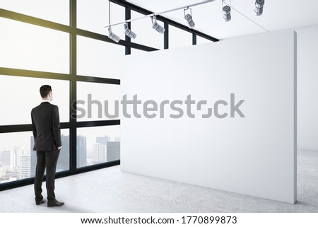 Businessman standing in clean gallery interior with copy space on white wall. Presentation concept. Mock up,