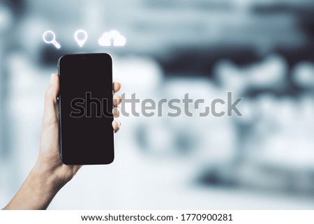Hand holding mobile phone with blank screen and digital icons on blurry office background. Technology and innovation concept.