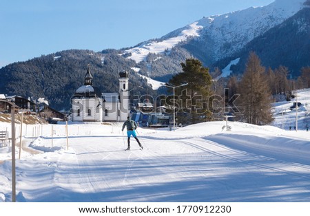 Cross-country skier on sunny track towards typical Austrian church, Seefeld, Austria