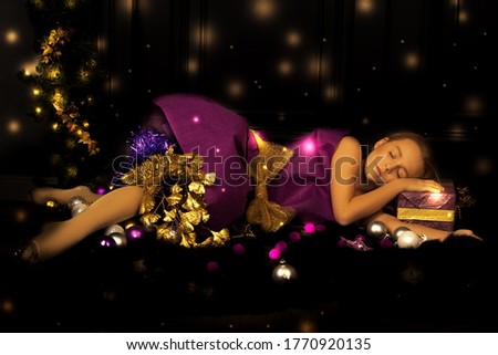 Photo of a little beautiful girl in a smart dress sleeps on Packed gifts for the new year. Magic lights and dreams. Fairy tale. Merry Christmas card or greeting in social networks