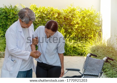 The doctor is helping to lift the patient out of the wheelchair while walking in the garden for physical therapy after the car accident. Concept of being by side and encouraging.