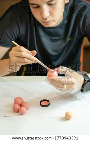 Young man paints a rubber ball in pink color. A hand in protective gloves painting the balls. Men's hands hold a detail and brush and paint the balls pink