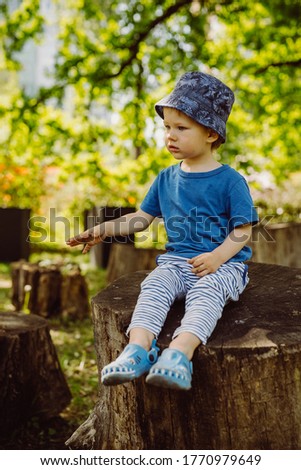 Two years old boy with blue t-shirt and blue hat eating apple in park.