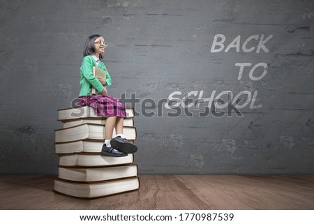 Asian little girl with eyeglasses sitting on the stack of books. Back to School concept