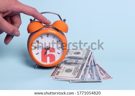 Close-up hand turns off the alarm, banknotes on a blue background. Work while they sleep