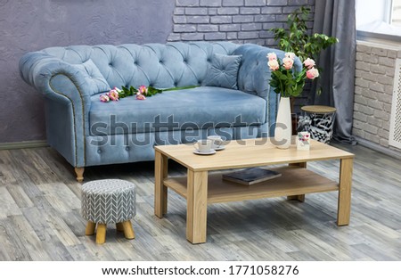 Spacious cozy grey living room with gray laminate on the floor. Wooden coffee table with a vase of flowers, cups, a picture on a gray wall.