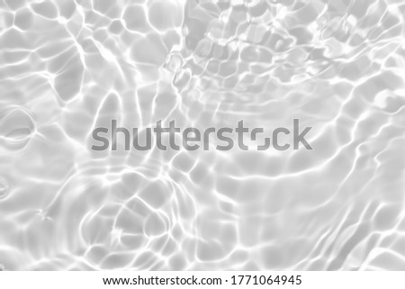 Closeup of desaturated transparent clear calm water surface texture with splashes and bubbles. Trendy abstract nature background. White-grey water waves in sunlight.