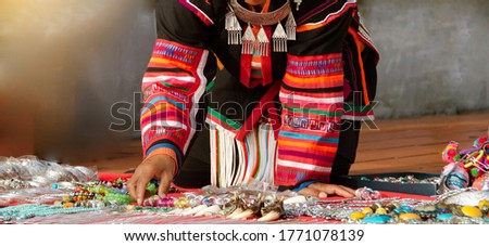 Women wearing colorful tailor-made clothes in northern Thailand, wearing large pieces of silver jewelry, are selling beautiful, colorful stone beads placed on fabric on the floor.