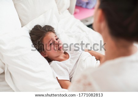 A small child is a girl, lying in bed and crying violently. Mother comforts the child. Taken from behind a woman. Concept of comfort and support for a child in a difficult situation. Royalty-Free Stock Photo #1771082813