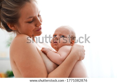 Mother's happiness! A loving mother hugs her baby after feeding, in the morning in the room. The mother looks at the adored baby. They are together. The concept of motherhood.