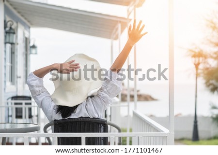 Summer vacation lifestyle with young girl wearing sunscreen hat on sunny day relaxing taking it easy happily sitting on the porch at beach-house on beach front celebrating healthy living life quality Royalty-Free Stock Photo #1771101467